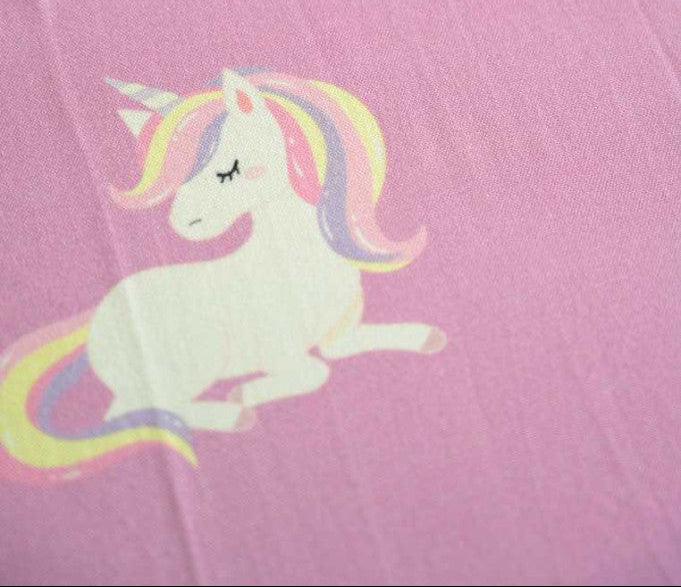 Pink fabric with a unicorn and rainbow design on a baby pink towel